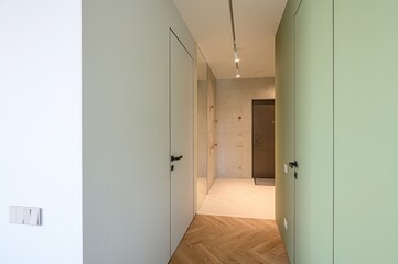 modern hallway with pastel doors, herringbone wood flooring, a mirror, and track lighting