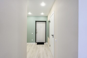well-lit hallway with light walls and wood-like flooring. A white door with a black frame and a second white door are visible