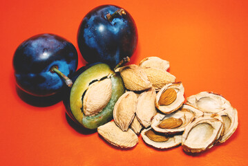 whole and cut plums with pits and plum pits on an orange surface