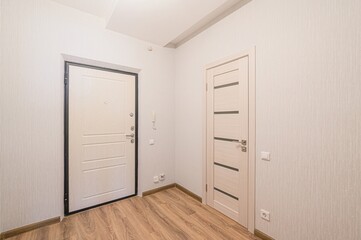 bright hallway with light wood floors, textured white walls, and a white front door with black trim. Another door stands to the side