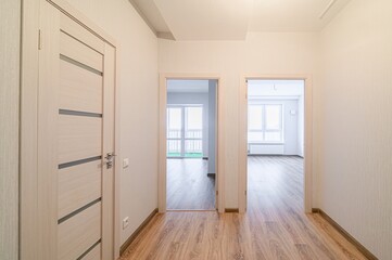 An interior shot of a hallway with two open doorways leading to rooms with windows. There's a...