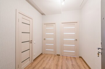 bright hallway with three light wood doors, each with horizontal panels. The walls are a soft white, and the floor is a light wood grain. A single light fixture is on the ceiling