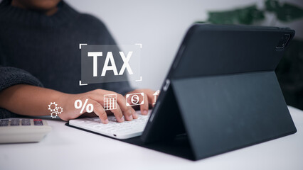Online tax calculation, financial planning, and digital accounting service. Person using tablet and keyboard with digital overlay of TAX, calculator, percentage, and money icons.