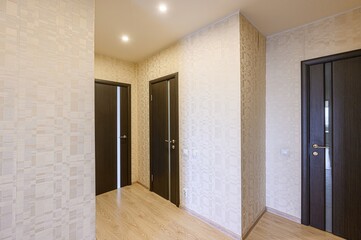 bright hallway features patterned wallpaper, wood-look flooring, and dark brown doors. The scene is illuminated by ceiling lights