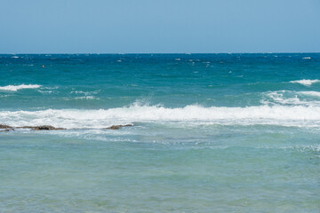 Scenic view of ocean waves crashing onto the shore under a clear blue sky. A tranquil seascape capturing the beauty of nature and the open sea