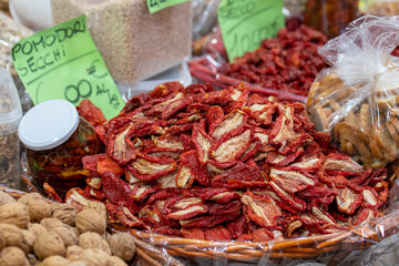 A large wicker basket filled with sun-dried tomatoes surrounded by glass jar of preserved tomatoes in oil in a traditional food market or artisanal display, showcasing Mediterranean cuisine