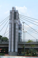 A modern concrete pylon supporting a cable-stayed bridge under a clear sky, with urban landscaping below.