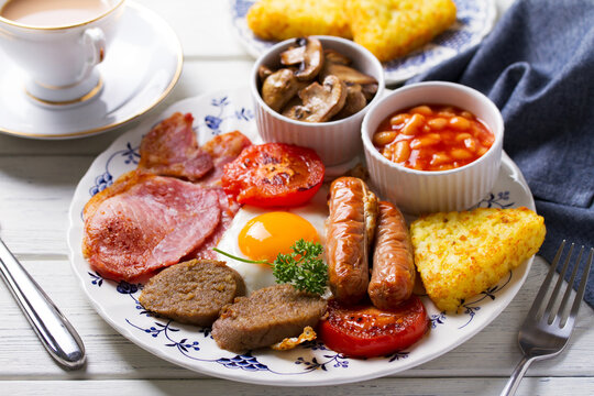 Full Irish or English breakfast with sausages, bacon, pudding, fried egg with runny yolk, hash browns, beans and tomatoes - Powered by Adobe