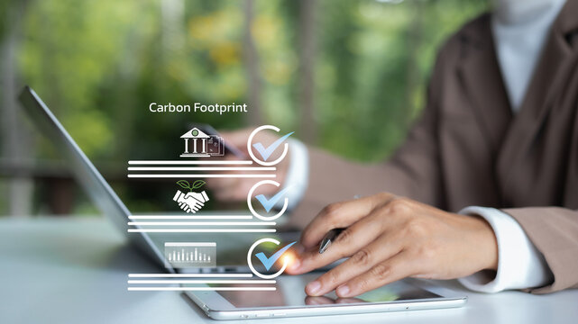 Businesswoman using tablet with carbon footprint checklist and digital icons. Concept of ESG reporting, sustainability strategy, green business, carbon reduction, and environmental analytics.