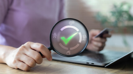 Magnifying glass highlighting green check mark on digital finance icons. Concept of online...