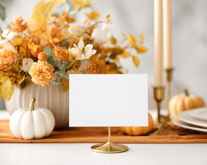 Blank card mockup on gold stand set on a festive table with pumpkins, candles and vibrant autumn flowers
