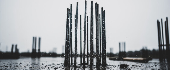 Metal rebar framework protrudes from water under an overcast sky at a construction site, evoking...