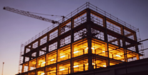 Building under construction with crane at dusk or dawn, silhouetted against a glowing sky and capturing the early or late hours of urban development progress.