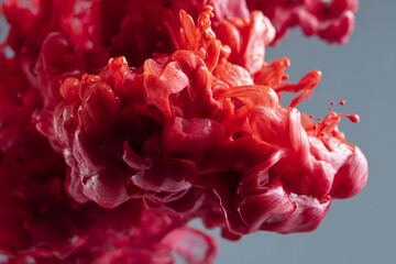 Abstract red ink swirling in water creating vibrant fluid shapes and textures against a soft gray background