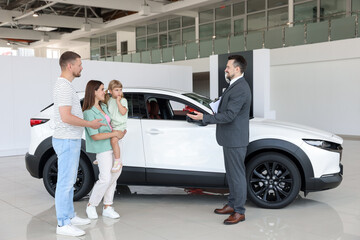 Smiling salesman with clipboard showing new car to family in salon