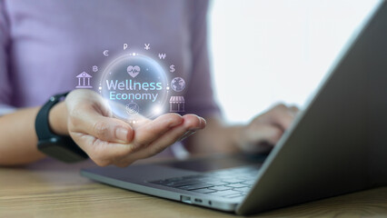 Hand holding virtual hologram of Wellness Economy icon with financial, health, and global business...