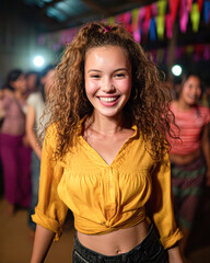 Fototapeta premium A joyful young woman with curly hair smiles brightly while dancing in a festive setting adorned with colorful decorations.