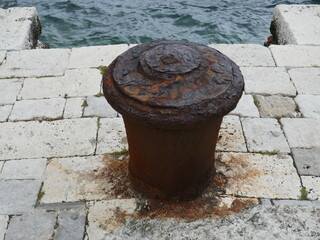 Naklejka premium Rusty old metal mooring bollard on stone dock by the ocean