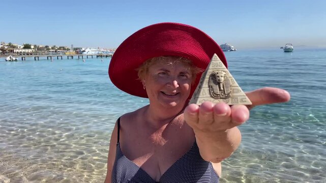Woman in swimsuit holding souvenirs of the pyramids in her hand on the sed background, tourism in Egypt concept, travel and vacation