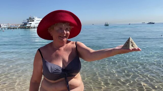 Woman in swimsuit holding souvenirs of the pyramids in her hand on the sed background, tourism in Egypt concept, travel and vacation