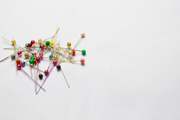 A pile of colorful head pins scattered on a white fabric background, commonly used for sewing or...