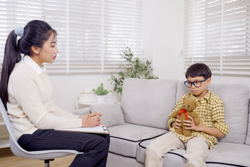 Asian female psychologist attentively listening to Asian boy during therapy session in mental...