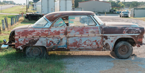 Passenger side of a very rusty 1950's car with parts removed in a small town in Texas