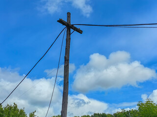 A weathered telephone pole stretches towards a vibrant blue sky filled with puffy clouds.