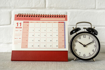 The calendar is for November 2025. A desktop calendar and a clock for planning on the table.
