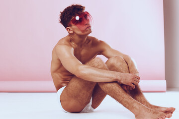 Stylish young man sitting on the floor, wearing bright sunglasses, showcasing a confident pose...