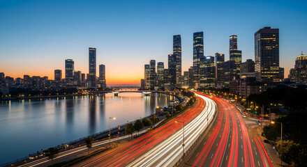 A bustling city skyline at dusk, with light trails from cars on a highway next to a river, reflecting the vibrant colors of the urban scene