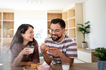 Happy couple enjoying waffles and milk for breakfast at home