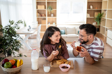 Happy couple enjoying breakfast with waffles and milk at home