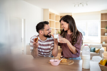 Happy couple enjoying breakfast with waffles and milk at home