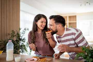 Happy couple sharing waffles with jam and milk at home