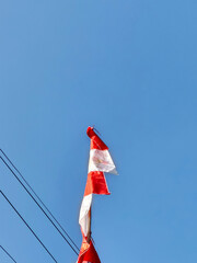 A tattered red and white national flag flying with pride against a vast clear blue sky, a symbol of freedom and resilience.