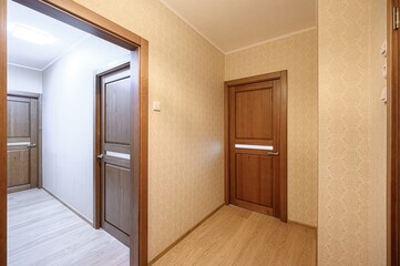 well-lit hallway with wooden doors, patterned wallpaper, and light-colored wood floors. Doors frame the view into adjacent spaces