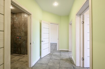 bright hallway with light green walls, gray tiled floors, and several doorways with white frames. One doorway leads to a shower area
