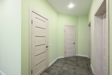 hallway painted light green, featuring three light wooden doors with modern designs and a dark tiled floor