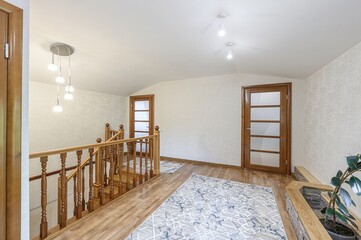 bright, airy hallway with wooden floors, stairs, and doors. A patterned rug covers the floor. A...