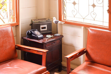The old radio with dial telephone and decorative doll on teak wood cabinet with leather chairs in...
