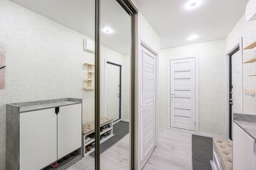 bright hallway with light walls, a large mirror, white doors, and furniture. The floor is light...