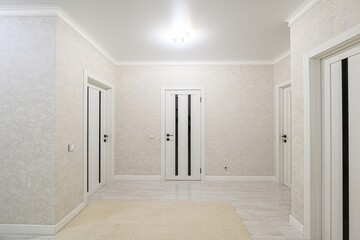 bright hallway features three white doors with black accents, light textured walls, a neutral rug, and a tiled floor, illuminated by a central ceiling light