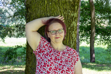 Smiling woman leaning against a tree trunk in the park