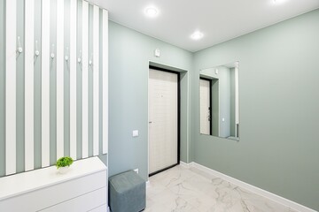 modern entryway with pale green walls, white marble floors, and white furniture accents. A mirror reflects the door, and a striped accent wall adds visual interest