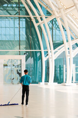 A male airport janitor mopping the floor to maintain the cleanliness of the airport area.