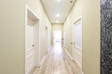 long hallway with wooden floors, light green walls, and white doors. Recessed lighting illuminates the space