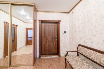 hallway with tiled floor, floral wallpaper, and wooden furniture. There's a mirrored closet, a wooden door, and a bench. The style looks classic and cozy