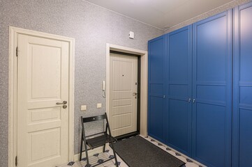 well-lit hallway features white doors, a blue wardrobe, textured gray walls, and patterned floor...