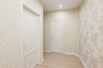 bright hallway with two white doors, patterned wallpaper and wooden floor. The space is well-lit, creating a clean, modern feel